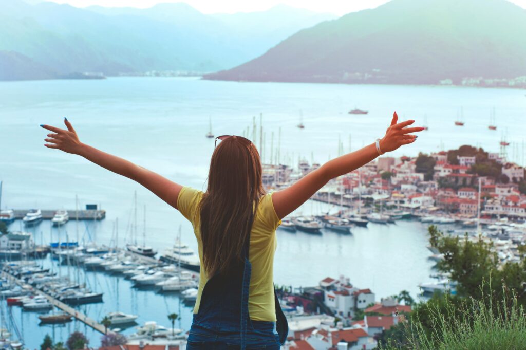 pexels-photo-1007901-1007901 A woman with open arms enjoys a scenic summer view of Marmaris harbor and yachts.